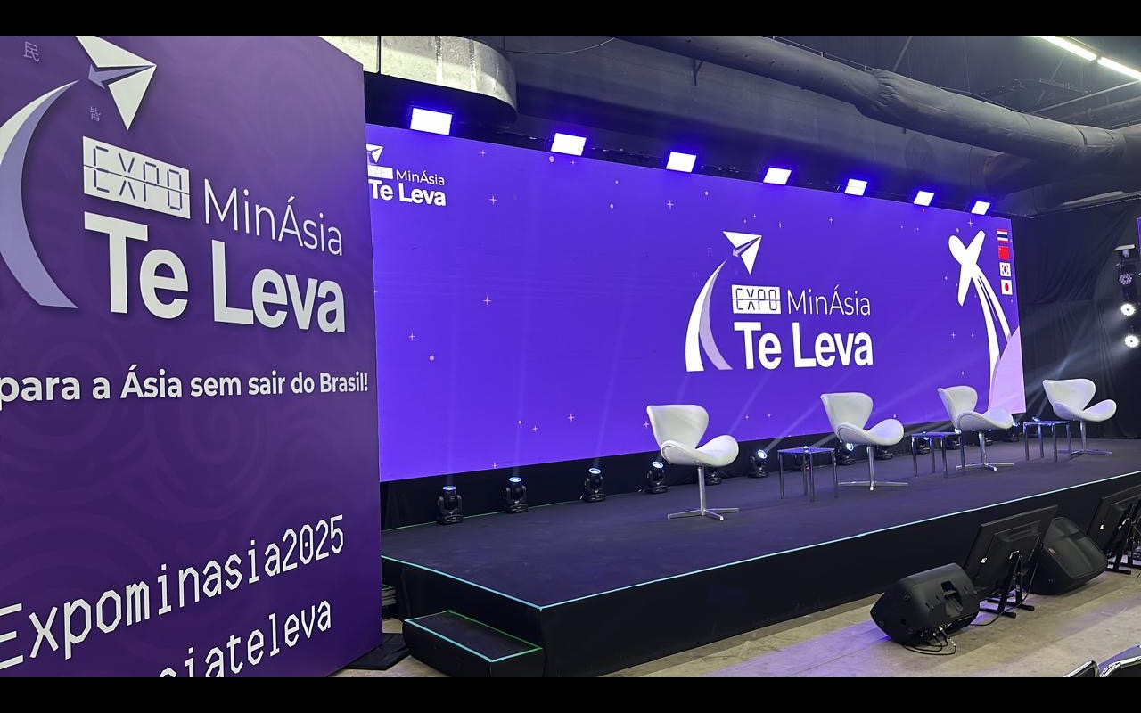 Palco elevado com parede de LED roxa, quatro poltronas brancas e refletores no piso, sob dutos aparentes do teto