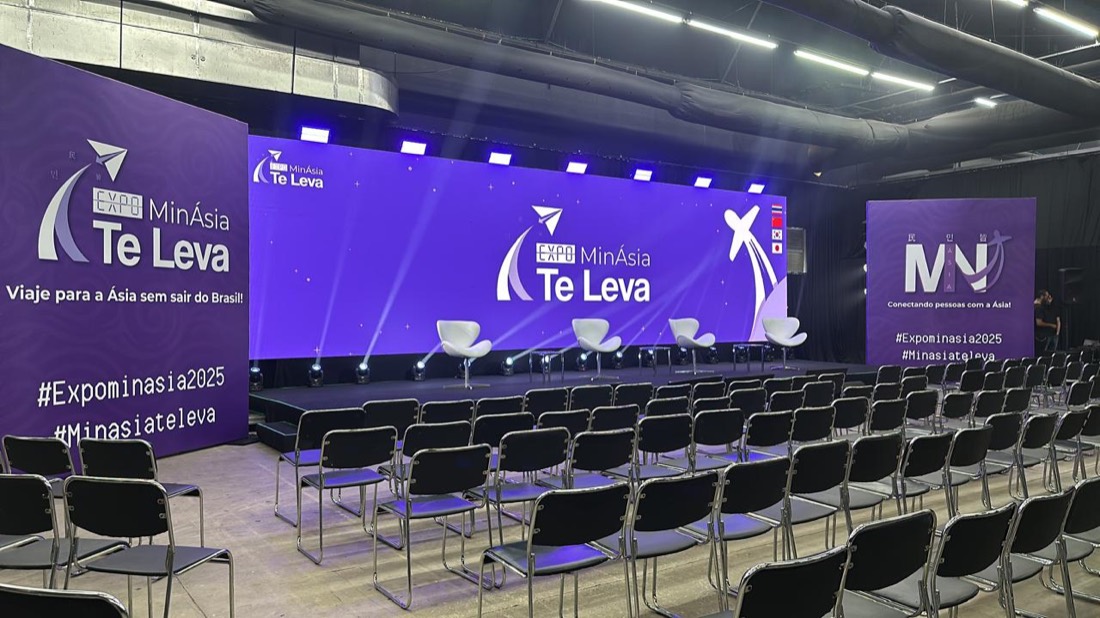 Plenária montada em galpão industrial, com teto de concreto aparente, dutos à vista e piso de concreto, servida por painel de LED e iluminação cênica própria